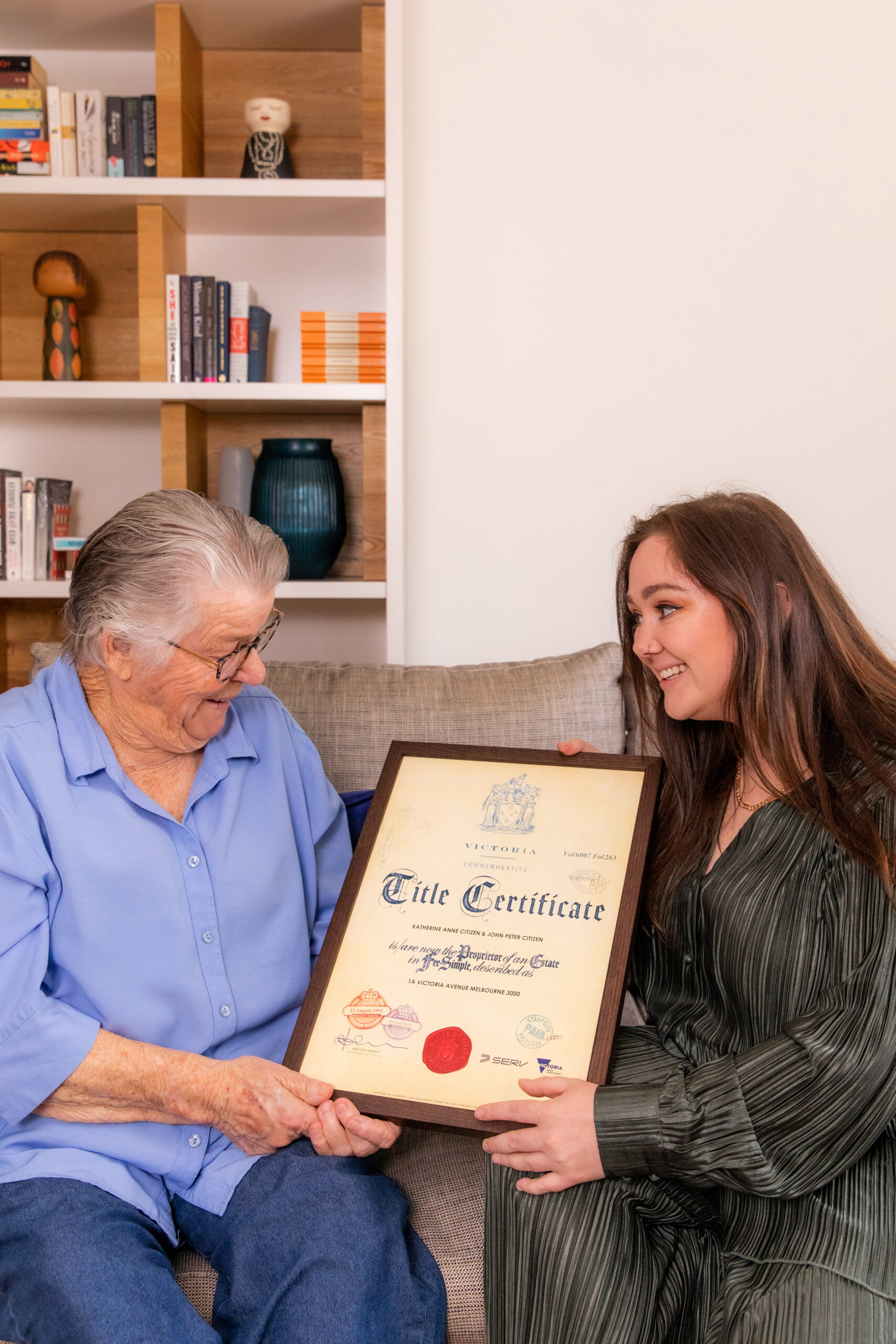 A granddaughter is gifting her grandmother a Commemorative Title. Both are similng