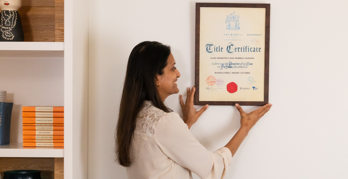 Woman smiling while hanging Commemorative Title on her wall as her frequently asked questions have been answered